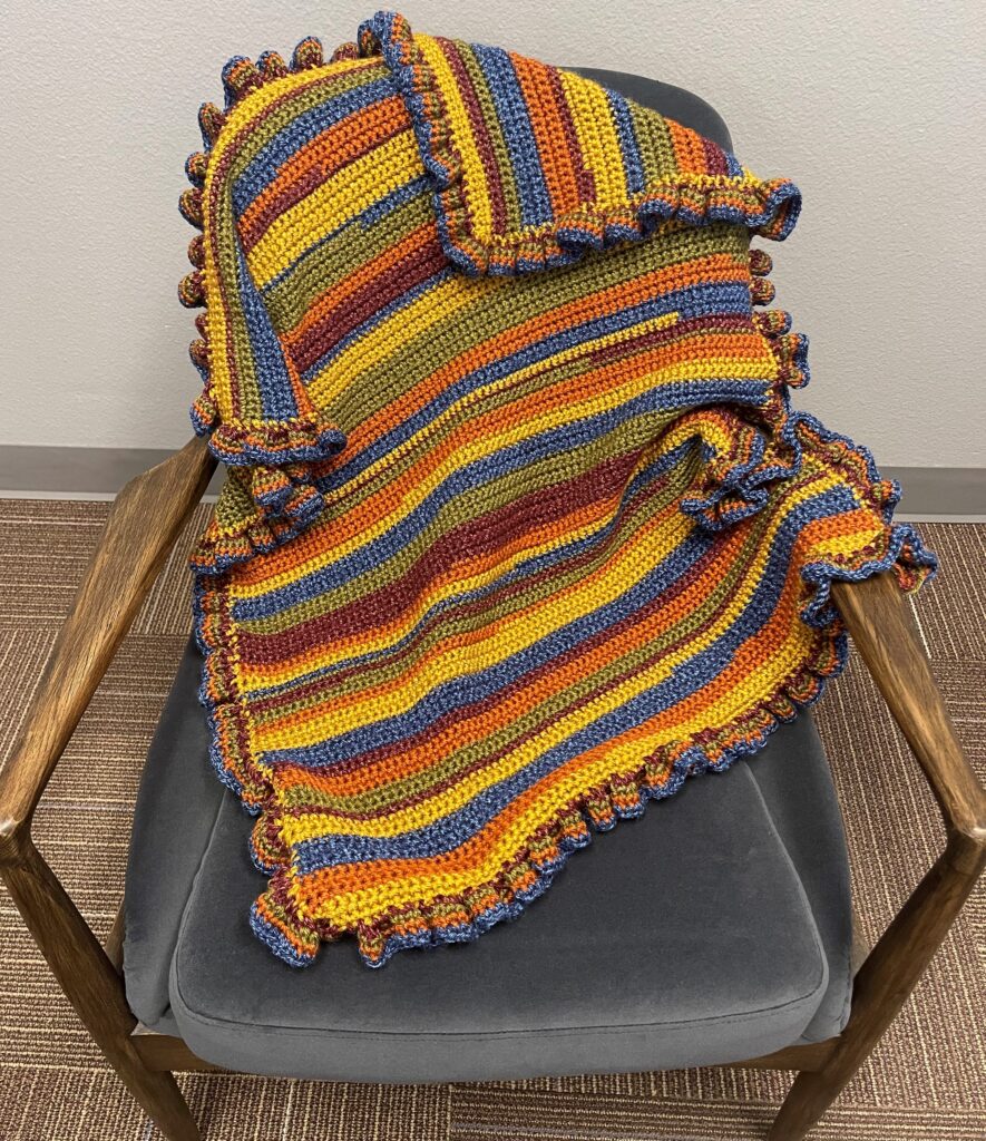 staggered crochet baby blanket draped over a sitting chair in an office environment