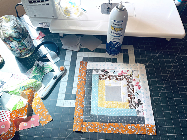 finished log cabin quilt block on cutting mat with sewing supplies