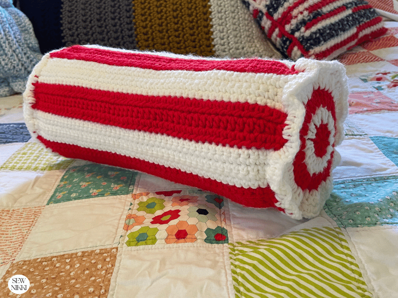 Finished candy cane stripe pillow sitting on quilt by Sew Nikki