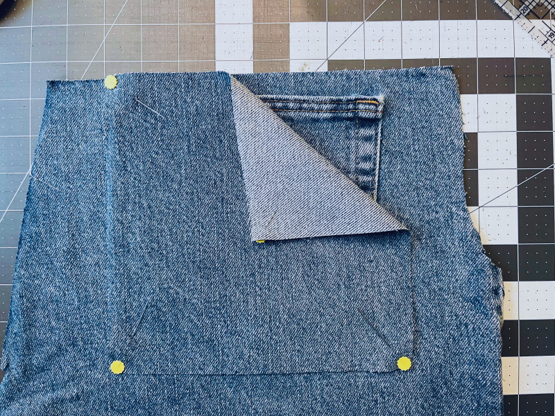 Measuring denim squares on cutting matt with sewing pins