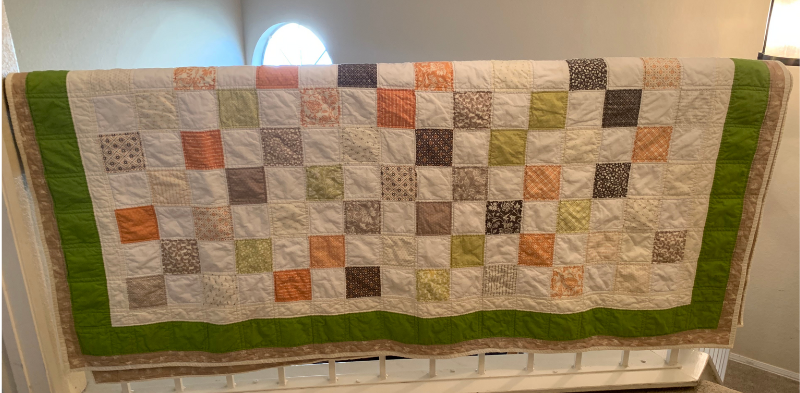 Finished charm square quilt handing on railing
