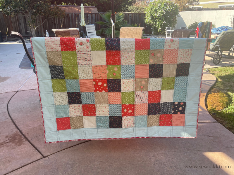 5" charm pack quilt with border displayed over patio chairs in backyard