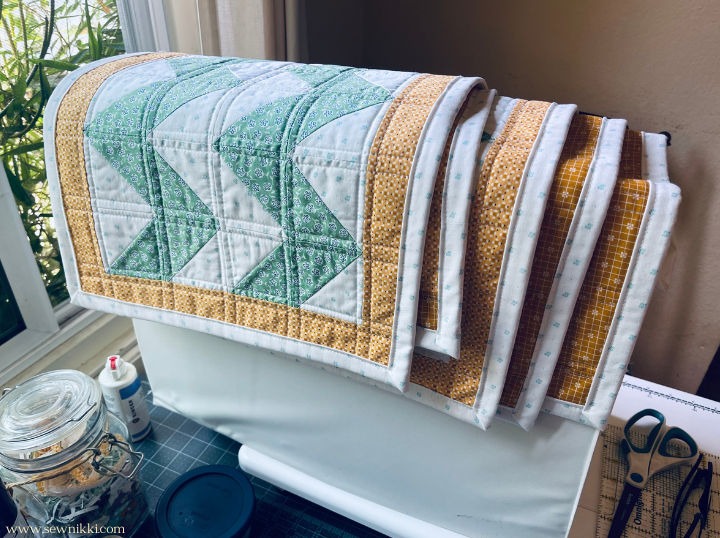 Chevron quilt pattern - stack of completed placemats hanging over sewing machine by Sew Nikki