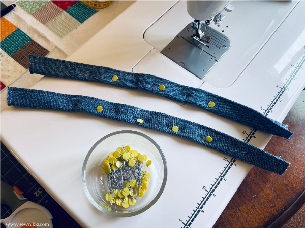 denim bag handles pinned with sewing pins sitting on sewing machine extension table
