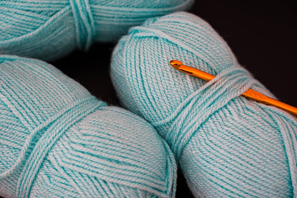 Close-up of teal yarn and an orange crochet hook, showcasing textile texture.