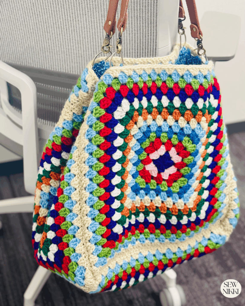 The Weekender Bag Crochet Shoulder Bag Pattern by Sew Nikki finished and hanging off a chair.
