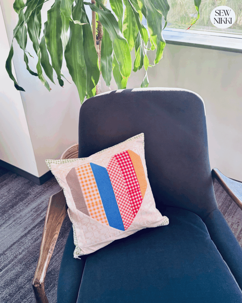 Free Patchwork Heart Block Pillow sewing pattern by Sew Nikki sitting on blue chair.
