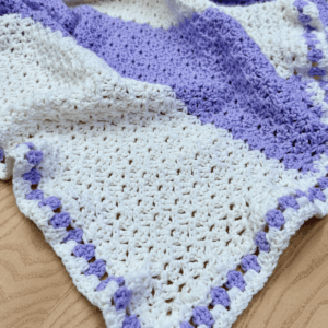 One row crochet lap blanket free pattern by Sew Nikki with big stripes and granny stitch border.