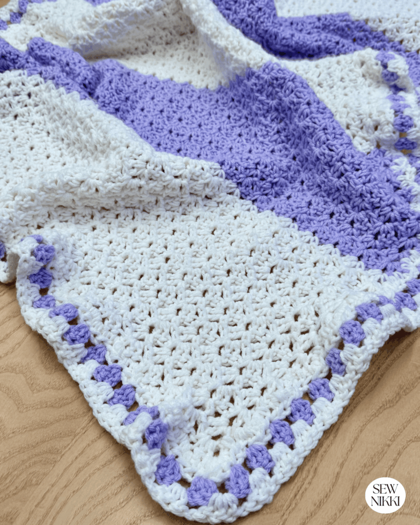 One row crochet lap blanket free pattern by Sew Nikki with big stripes and granny stitch border.