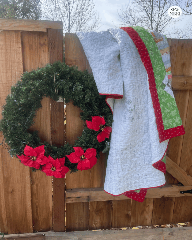 Christmas quilts make great gifts for the holidays or any time of year - on point scrappy log cabin quilt draped over fence with Christmas wreath.